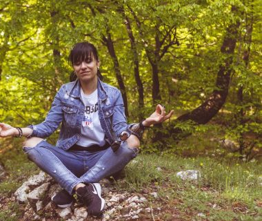 A woman meditates peacefully in a lush green forest, exuding calm and relaxation.